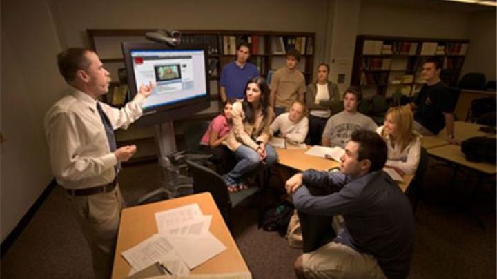 A university professor gives a presenation on a computer to a classroom of college students.