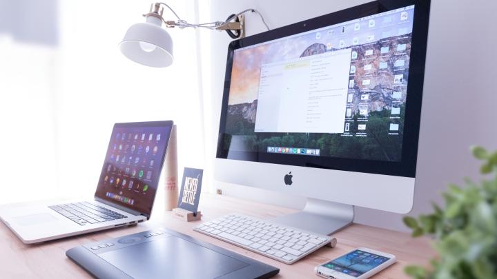 A desktop, laptop, and cellphone on a desk.