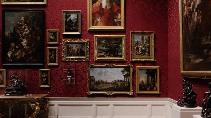 A museum wall covered in old paintings with gold frames.
