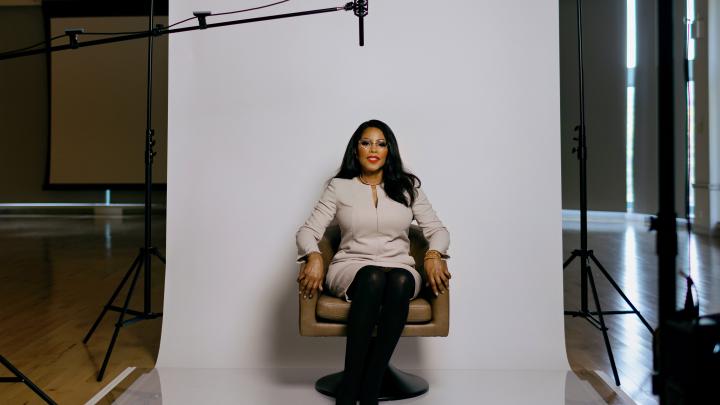 Ilyasah Shabazz sitting in a brown chair in front of a white background with a boom microphone above her.