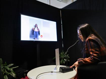 An exhibit with the Lora King Interactive Interview on a TV while someone asks a question into a microphone.