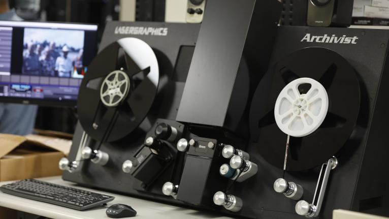 A film scanner with reels and a computer monitor displaying the digitization process.